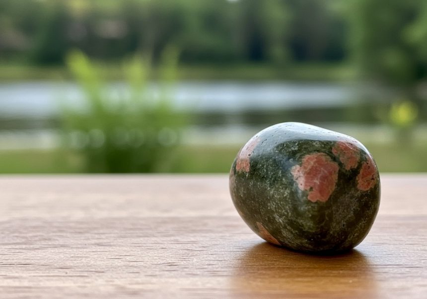 Cristalul Unakit, cu nuanțe verzi și roz, pe o masă de lemn.