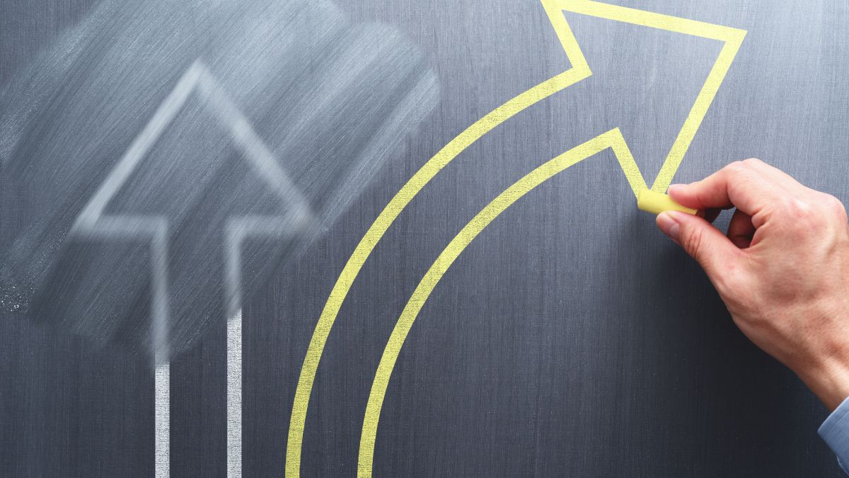 O mână desenează o săgeată galbenă pe un fundal gri, simbolizând schimbarea.