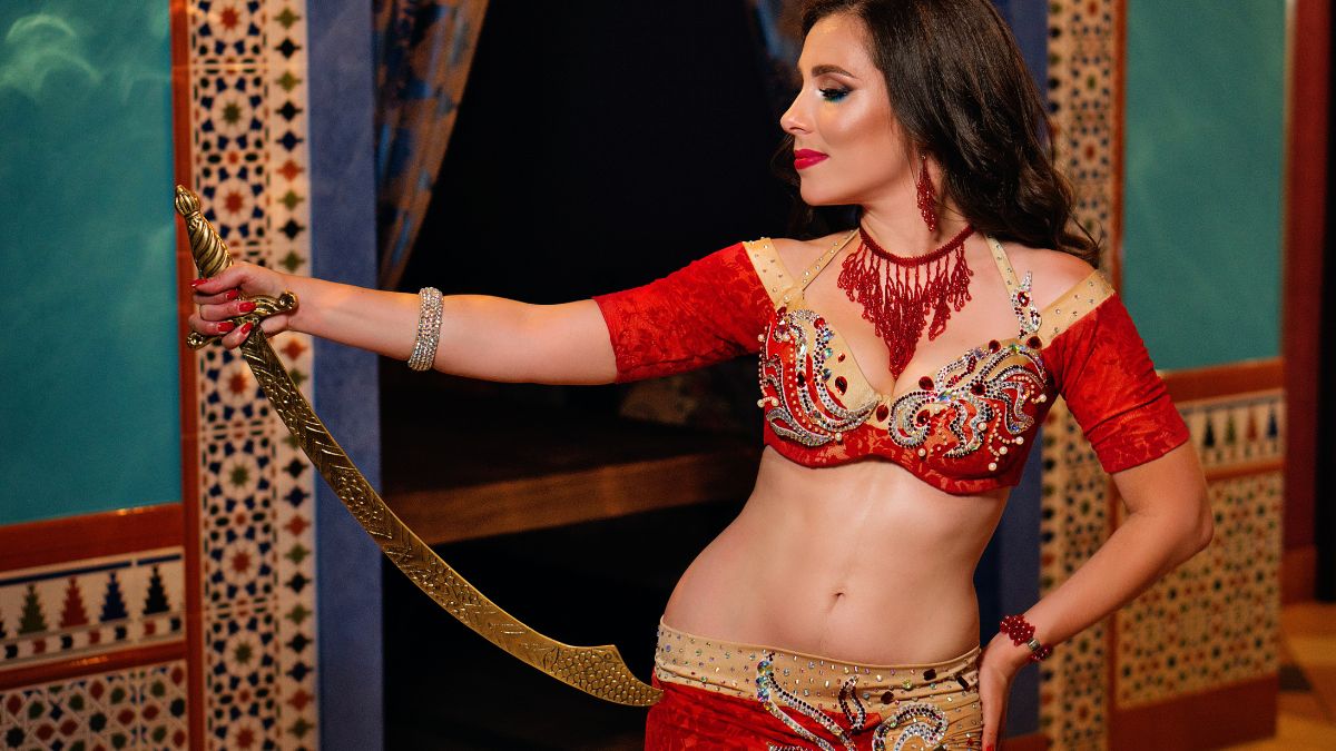 O dansatoare orientală îmbrăcată în costumul tradițional roșu, ținând o sabie.