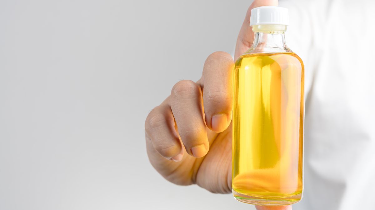 O sticlă de liniment scabicid, cu lichid galben, ținută de o mână.