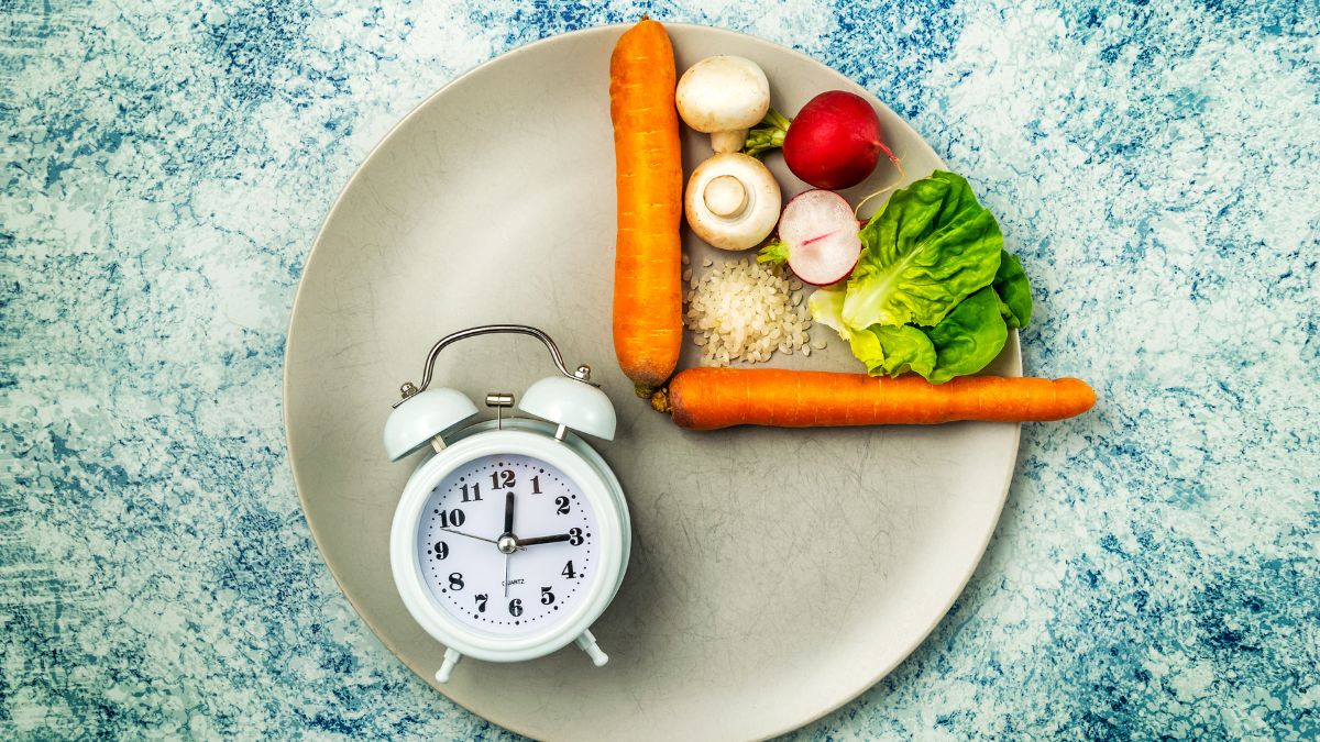 O farfurie cu legume proaspete, orez și un ceas deșteptător, simbolizând postul intermitent.