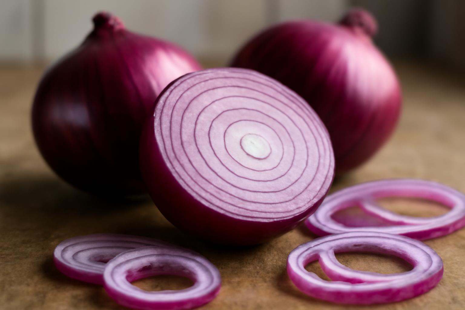 Ceapă roșie tăiată, cu inele și două cepe întregi în fundal.