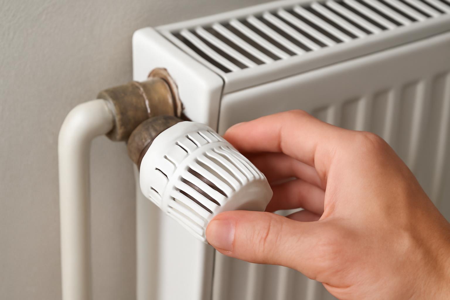 O mână ajustează un cap termostatic pe un radiator alb, eficiență energetică.