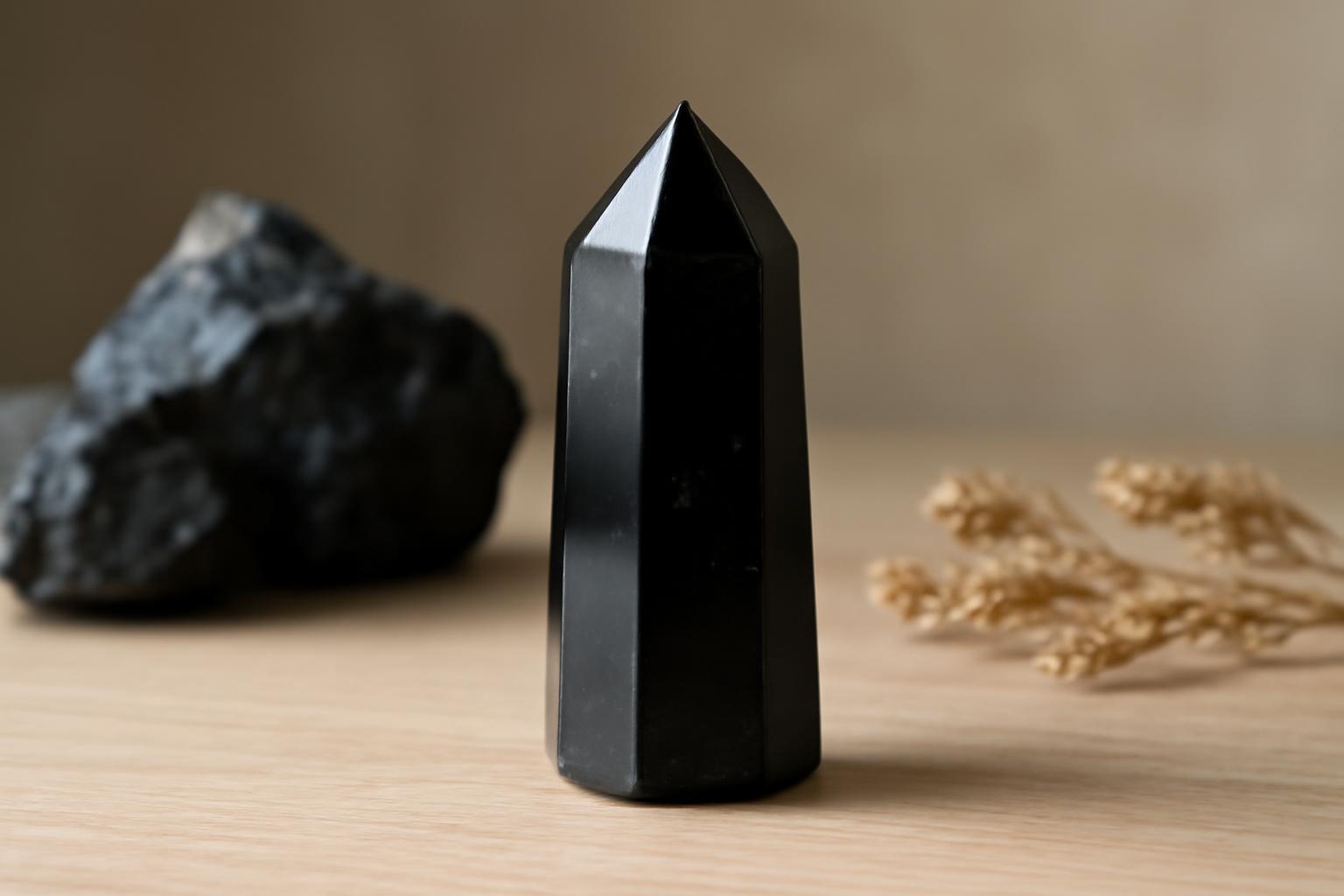Un cristal de obsidiană neagră cu vârful ascuțit, pe un fundal natural.